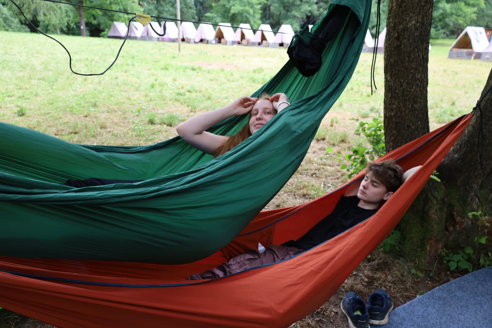 Dva účastníci odpočívají v hamakách na kraji tábořiště